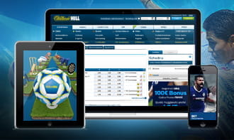 Un laptop, uno smartphone e un tablet che mostrano l'app di William Hill e un pallone da calcio con il logo dell'operatore